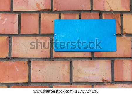 A blank blue plate is screwed to a brick wall.