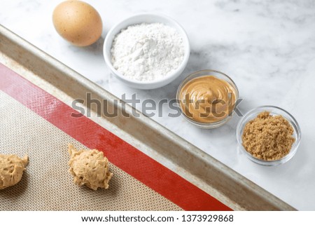 Flat lay of recipe ingredients for peanut butter cookies,  beside raw dough balls, on a white marble counter 