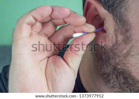 a man with a beard cleans his ears with a cotton swab to clean