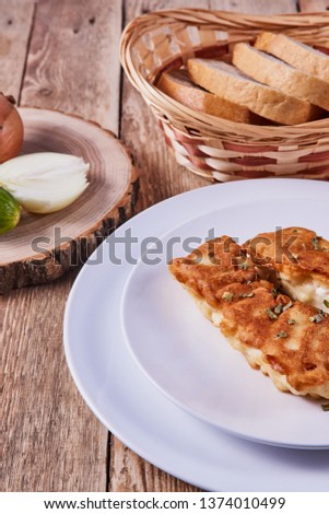 Deep-fried battered cod fillets, in a white plate next to onions, cucumber and bread on a wooden background. Close-up