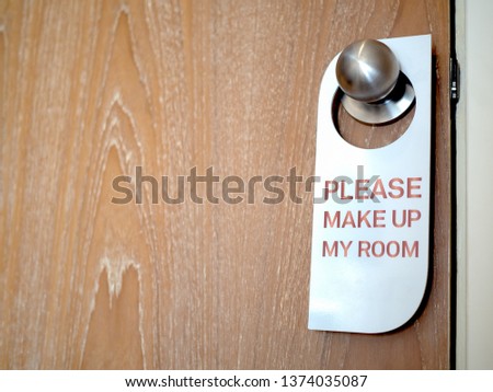 Closed wooden door of hotel room with please make up my room sign hanging on the stainless steel door knob with copy space.