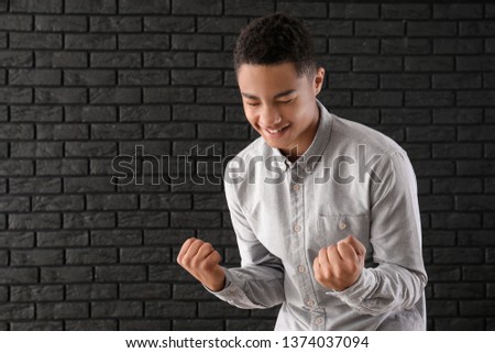 Portrait of happy African-American teenage boy on dark brick background