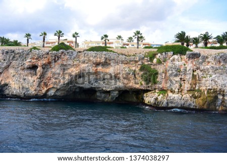 The view from the boat on the sea walk to the caves under the rocky shore of the blue transparent Mediterranean Sea and the rocky shore with palm trees. East coast of the Spanish island of Mallorca