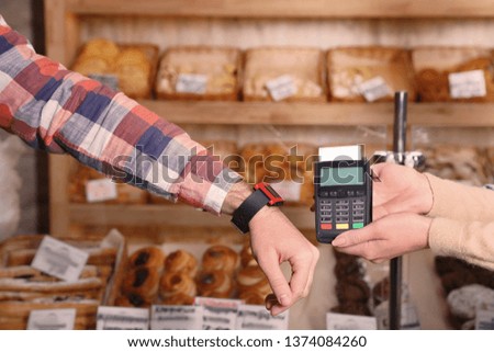 Man using terminal for contactless payment with smart watch in bakery, closeup