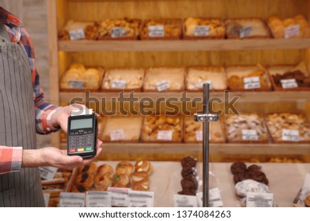 Man holding payment terminal in bakery, closeup. Space for text