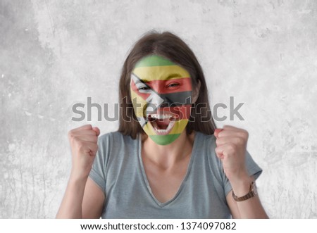 Young woman with painted flag of Zimbabwe and open mouth looking energetic with fists up