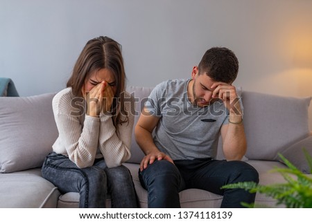 Sad pensive young girl thinking of relationships problems sitting on sofa with offended boyfriend, conflicts in marriage, upset couple after fight dispute, making decision of breaking up get divorced 