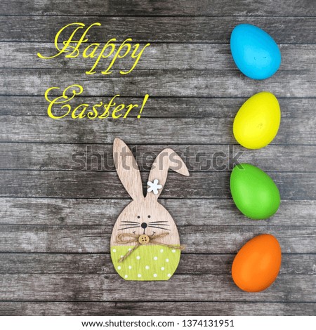 Colored Easter eggs and bunny at wooden table with text Happy Easter.