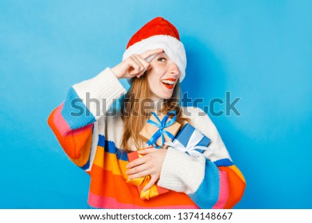 A young girl in a Santa Claus hat is holding gift boxes on a blue background. The concept of New Year and Christmas, gifts for the winter holidays, shopping at sales.