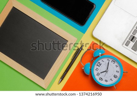 colored background, black board, clock, pen, smartphone and a laptop