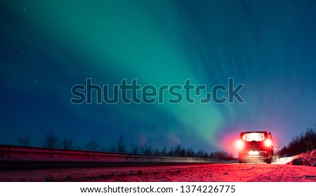 the car is standing on the side of the road, in the sky there are horses and aurora borealis. place for text.