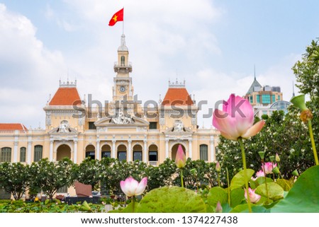 Saigon City Hall (or Ho Chi Minh City People's Committee) with pink lotus flowers and blooming plumeria trees in the foreground (blurred). One of the top tourist attractions of the city. Vietnam.