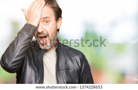 Middle age handsome man wearing black leather jacket surprised with hand on head for mistake, remember error. Forgot, bad memory concept.