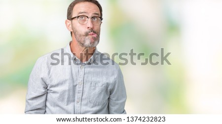 Handsome middle age elegant senior man wearing glasses over isolated background making fish face with lips, crazy and comical gesture. Funny expression.