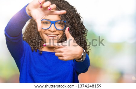 Young beautiful woman with curly hair wearing glasses smiling making frame with hands and fingers with happy face. Creativity and photography concept.