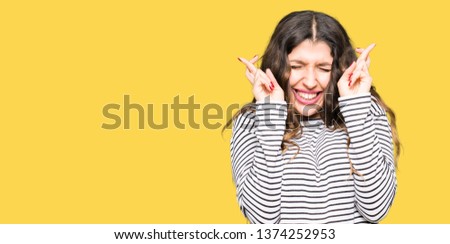 Young beautiful woman wearing stripes sweater smiling crossing fingers with hope and eyes closed. Luck and superstitious concept.