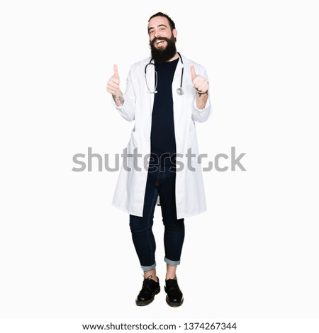 Doctor with long hair wearing medical coat and stethoscope success sign doing positive gesture with hand, thumbs up smiling and happy. Looking at the camera with cheerful expression, winner gesture.