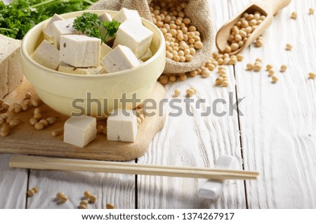 Soy Bean curd tofu in clay bowl and in hemp sack on white wooden kitchen table. Non-dairy alternative substitute for cheese. Place for text