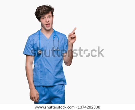Young doctor wearing medical uniform over isolated background with a big smile on face, pointing with hand and finger to the side looking at the camera.