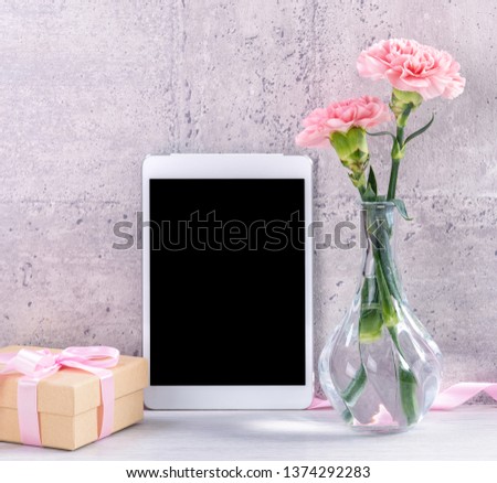 Home decor with blooming carnation and tablet as photo frame beside wall on the table - Close up, copy space, mock up, beautiful mothers day concept.