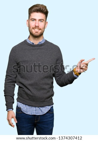 Young handsome elegant man with a big smile on face, pointing with hand and finger to the side looking at the camera.