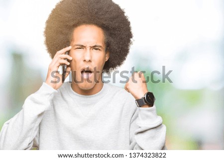 Young african american man with afro hair talking on smartphone annoyed and frustrated shouting with anger, crazy and yelling with raised hand, anger concept