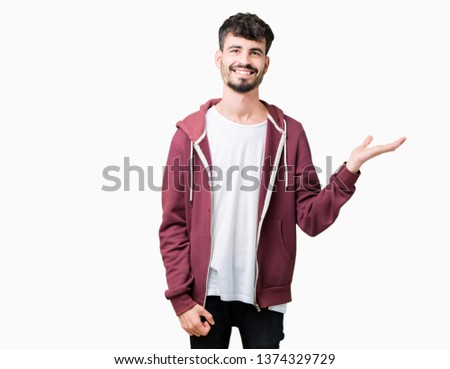 Young handsome man over isolated background smiling cheerful presenting and pointing with palm of hand looking at the camera.