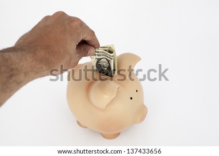  man's hand saving money, dollars in piggy bank