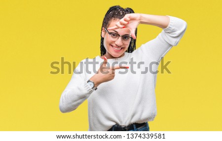 Young braided hair african american girl wearing glasses and sweater over isolated background smiling making frame with hands and fingers with happy face. Creativity and photography concept.