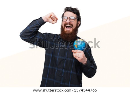 Young bearded man won a world trip, vacation concept. Man celebreating and holding a globe