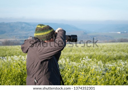 Nature photographer in winter equipment in a green field. Camera ready to shoot.