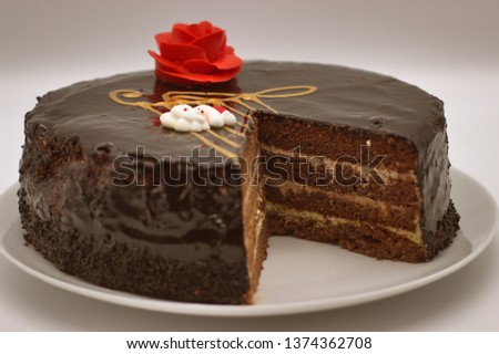 Chocolate cake on a white background. Image from above. The cake is decorated with a red flower of cream and a stylized musical style with a G-Clef