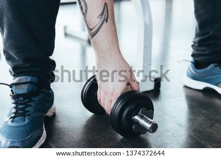 cropped view of Overweight tattooed man in trainers exercising with dumbbell at gym