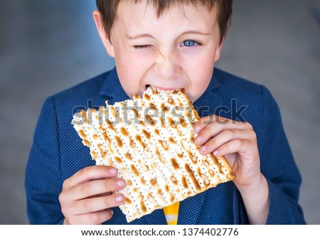 Cute Caucasian Jewish boy squinting and  taking a bite from a traditional Jewish matzo unleavened bread. Jewish Passover Pesach concept image. Pesach child stock image.