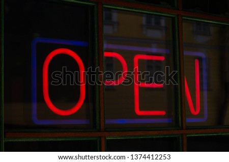 A red neon sign on a dark window with the word open.