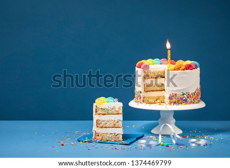 Sliced confetti Birthday cake  with lit candle, colorful icing and Sprinkles over a blue background.