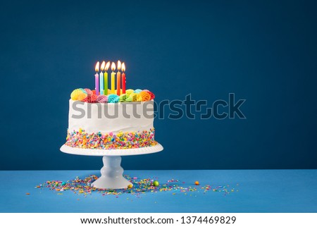 Birthday cake with rainbow icing, colorful Sprinkles and lit candles over a blue background. Royalty-Free Stock Photo #1374469829