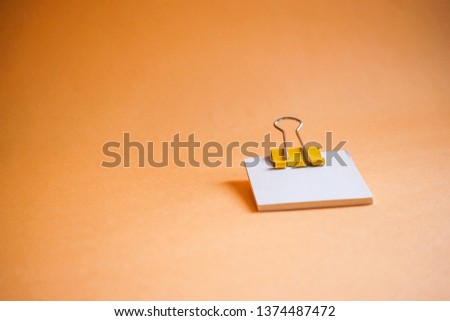 Yellow paper clip and blank paper on a orange background