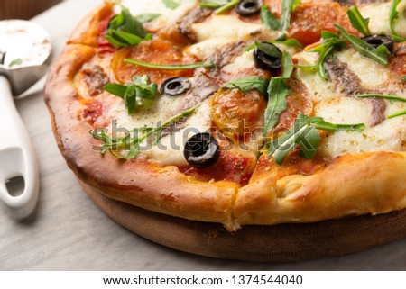Delicious pizza with mozzarella, rocket, black olives, tomato sauce and anchovies