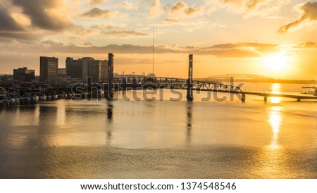 Cityscape aerial view of The Main Street Bridge, also known as John T. Alsop Jr. Bridge, in downtown Jacksonville Florida with other bridge in background during the bright glow orange of sunrise.