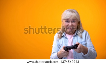 Active optimistic elderly woman playing computer game, holding joystick, gadget