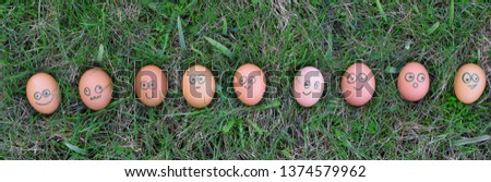 Nine easter eggs with different facial expressions on painted faces lying in row in spring grass outdoors, panoramic top view.

