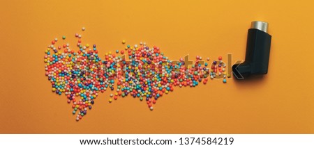 Black asthma inhaler with particle aerosol spay made by color preparations (vitamins, dyes, flavor enhancers, nutritional supplements, innovative technologies, candy sweets)  on a orange background. 