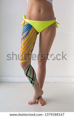 kinesiotaping the legs of the girl standing in front of a white wall in the Studio with colored stripes