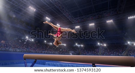 Female athlete doing a complicated exciting trick on gymnastics balance beam in a professional gym. Girl perform stunt in bright sports clothes Royalty-Free Stock Photo #1374593120