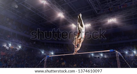 Male athlete doing a complicated exciting trick on horizontal gymnastics bars in a professional gym. Man perform stunt in bright sports clothes