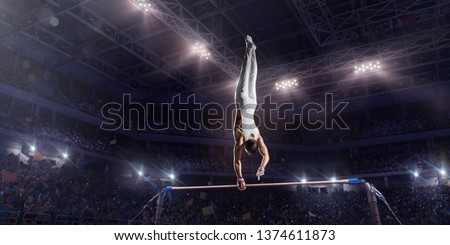 Male athlete doing a complicated exciting trick on horizontal gymnastics bars in a professional gym. Man perform stunt in bright sports clothes
