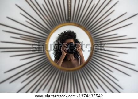 Black woman holding a professional camera taking a picture of her reflection on the mirror
