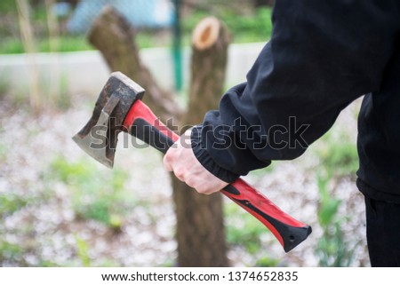 Male hand holding an axe stuck in a wooden pencil case. Man is chopping wood with axe. A man with an ax in his hand