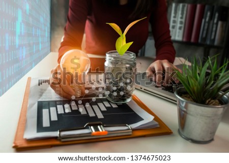 Business woman hand holding lightbulb with money stack and accounting finance in office, Finance And Investment Concept.